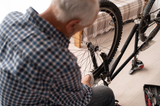 Old Cyclist Fixing Bicycle Wheel After Service in Home Living Room