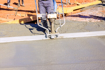 Workers are using concrete leveling tool to smooth out freshly poured cement at construction site.