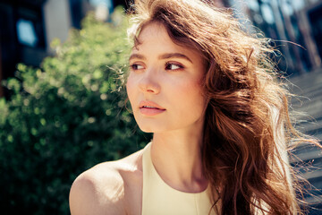 Beautiful young woman outdoors on a sunny day with flowing hair wearing a chic yellow dress
