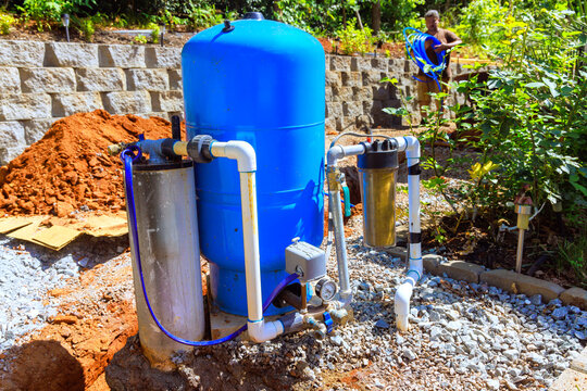 Workers set up artesian water well system in garden surrounded by gravel
