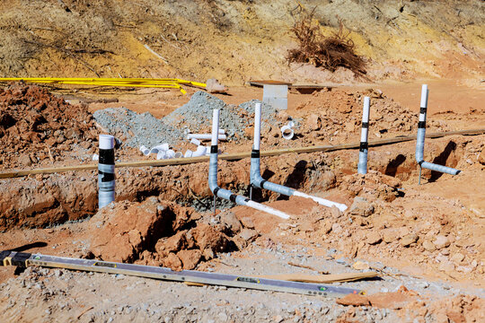 Wastewater plumbing pipes are positioned in freshly excavated area at construction site during work day