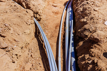 Workers install various electrical pipes in deep trench at construction site
