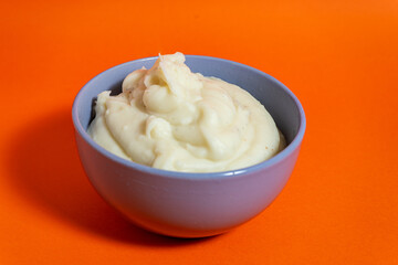 Creamy mashed potatoes served in a bowl on vibrant orange background