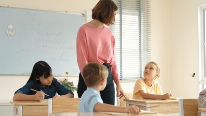 Energetic smart teacher explain classwork to caucasian boy at classroom while multicultural student...