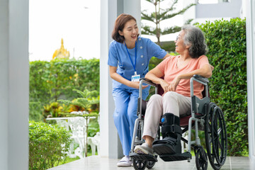 Fototapeta premium smiling Asian caregiver in scrubs enjoys a moment outdoors with senior woman in a wheelchair, pointing at nature enthusiasm. Concept of home healthcare, assisted living, and positive elderly support.
