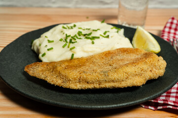 Breaded fish fillet with mashed potatoes and chives on a dark plate