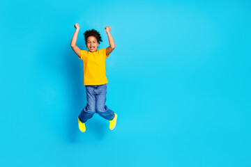 Obraz premium Joyful young girl jumping with raised arms against blue background wearing casual clothes