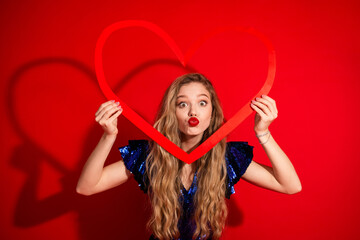 Naklejka premium Smiling young woman holding a heart shape while celebrating in a festive atmosphere