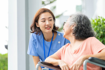 smiling Asian caregiver in scrubs enjoys a moment outdoors with senior woman in a wheelchair,...