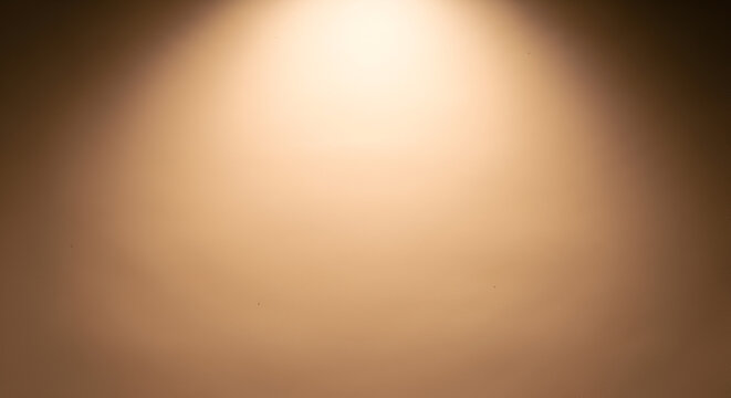Warm golden spotlight shining on a smooth brown gradient background. Abstract studio lighting concept for product display.