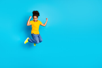 Obraz premium Energetic young girl in casual attire jumps joyfully against a vibrant blue background, expressing happiness and excitement.