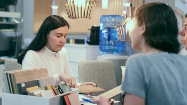 Female manager offers customers wood options for the kitchen. Consultant in a furniture salon offers wooden samples for the floor and laminate flooring. High quality 4k footage