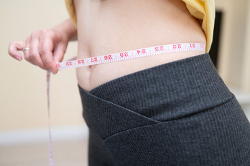 Close-up of a woman measuring her waist with a tape. She is wearing sporty clothes, symbolizing weight loss or fitness goals