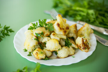 Fried cauliflower with spices and herbs on a green background