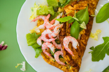Delicious omelette with shrimps and fresh greens on top, on a green background