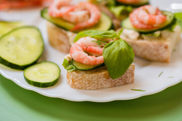 Minimalistic canapes with shrimps, lettuce and cucumber on a green background