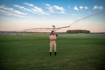 A farmer is watering irrigation farm. The Farmer on irrigation to water field. Farmer near Irrigation sprinkles water on grass. Irrigation system in action on the farm. Sprayer for watering field.