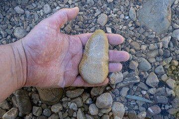 Adult hand holding a stone in clear river water