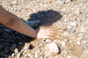 Child's hand digging stones in river water