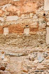 Old wall with rough brown mortar, exposed bricks, and mixed stones embedded in faded plaster,...