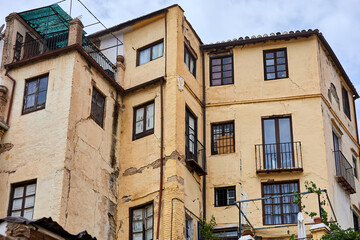 Old building with yellow stucco walls, cracked surfaces, wooden windows, small balconies, and tiled...