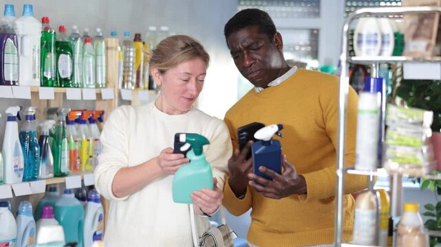 Woman with African husband examines product, scans QR code of paint remover spray. Client reads coupon download code with mobile phone camera. Customer checks absence of animal testing of product