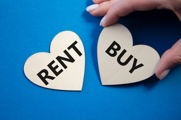 Rent or Buy symbol. Concept word Rent or Buy on wooden hearts. Businessman hand. Beautiful blue...