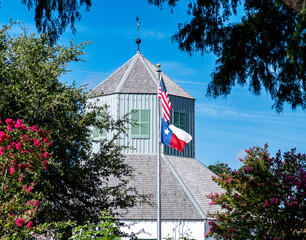 American flag over a Texas flag on a pole as viewed through the trees