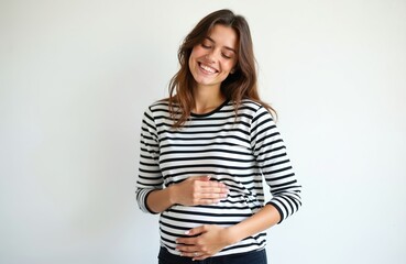 Obraz premium Young woman in striped t-shirt touches tummy, smiles gently. Beautiful female eats with satisfaction. Portrait on white background. Happy, joyful, smiling face, satisfaction. Pregnancy concept.