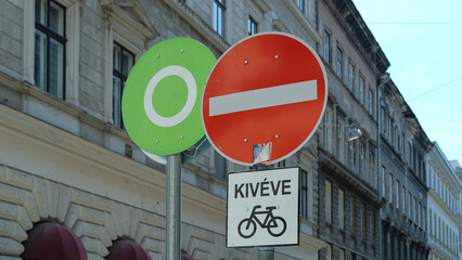 Street signs in an urban setting showing a no-entry sign and a green circle, with a Hungarian sign underneath allowing bicycles.