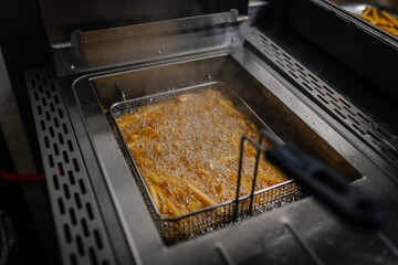 French fries being deep-fried in hot oil inside a commercial fryer in a professional kitchen.