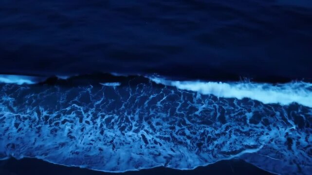 Bioluminescent blue waves crashing on shore at night