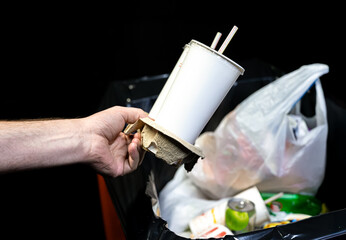 Close-up of a hand throwing disposable beverage cups into a trash bin. Symbol of modern urban...