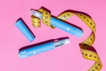 Healthcare concept with Ozempic pens and measurement tape. Pink setting emphasizes weight loss and...