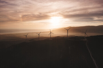 Wind turbines stand silhouetted against a breathtaking sunset, generating clean energy amidst rolling hills, extending to the distant horizon