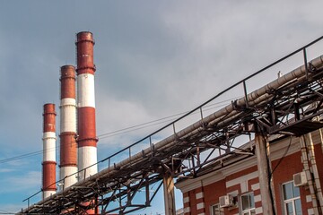 Three towering chimneys stand amidst interconnected pipelines against a cloudy sky