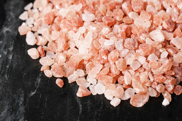 Pink Himalayan salt granules. Natural rock salt on black stone background. Healthy seasoning for...