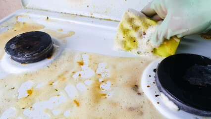 Housewife washes dirty gas stove with sponge and detergent with gloves, cleaning, cleaning soiled stove for cooking.