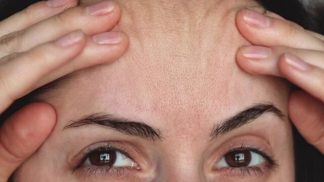 Close-up of a woman pulling the skin on her forehead to reveal fine lines and wrinkles. The image highlights facial aging, skin texture, and expression lines for skincare, dermatology, or beauty-relat
