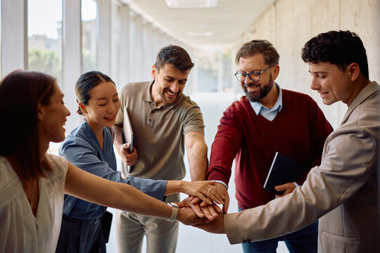 Happy diverse colleagues holding hands in unity while celebrating their business success in the office.