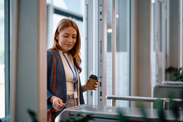 Smiling businesswoman using smart card while coming to work in the office.