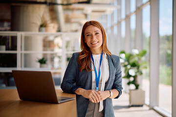 Happy female manager working on laptop at corporate office and looking at camera.