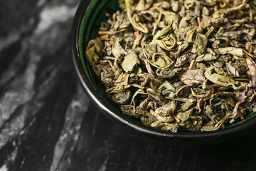 Dried green tea leaves. Loose leaf tea in ceramic bowl on dark marble background. Organic herbal...