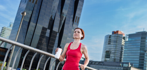 Woman resting after her morning workout, drinking water on a city bridge