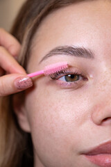 Caucasian woman brushing her eyelashes after lamination. 