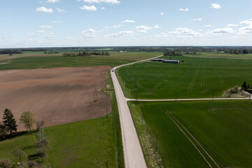 Expansive agricultural fields with plowed and green crops divided by a paved road. Scattered trees,...