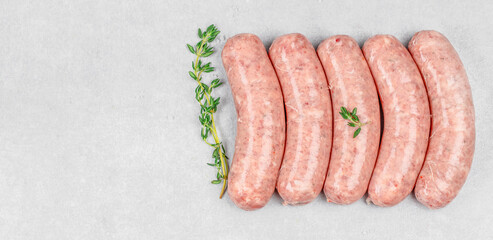 Fresh raw sausages neatly arranged with sprigs of thyme on a clean light gray surface, ideal for...