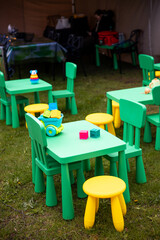 Green tables, yellow stools, and toys like blocks and a toy train are arranged on grass under a...