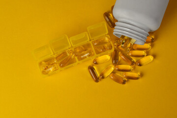 Organizer with Omega-3, Omega-9 capsules and a white bottle from which the capsules are poured out,...