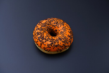 donut in orange glaze with chocolate sprinkles on black background
